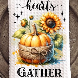 May include: White waffle-textured kitchen towel with a watercolor design featuring a pumpkin wrapped in burlap, sunflowers, and the text "THANKFUL hearts GATHER here". The design has a fall theme.