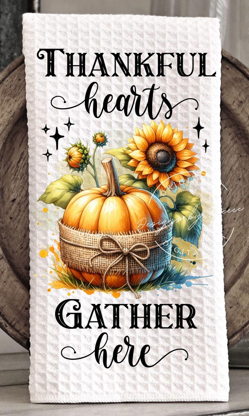 May include: White waffle-textured kitchen towel with a watercolor design featuring a pumpkin wrapped in burlap, sunflowers, and the text "THANKFUL hearts GATHER here". The design has a fall theme.