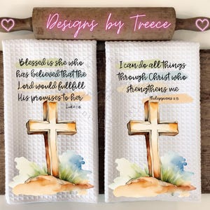 May include: Two white kitchen towels with watercolor cross designs and inspirational bible verses. The first towel reads "Blessed is she who has believed that the Lord would fulfill His promises to her Luke 1:45". The second towel reads "I can do all things through Christ who strengthens me Philippians 4:13".