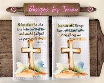 May include: Two white kitchen towels with watercolor cross designs and inspirational bible verses. The first towel reads "Blessed is she who has believed that the Lord would fulfill His promises to her Luke 1:45". The second towel reads "I can do all things through Christ who strengthens me Philippians 4:13".
