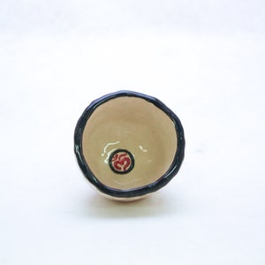 May include: A small, white ceramic bowl with a black rim and a red Om symbol in the centre.