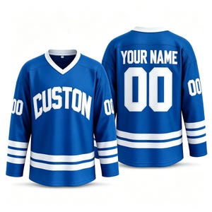 Op de afbeelding: Een blauw ijshockey-shirt met witte accenten, voorzien van de tekst CUSTON op de voorzijde en YOUR NAME met het nummer 00 op de achterzijde. De mouwen tonen het nummer 00 en het kledingstuk heeft twee horizontale witte strepen bij de zoom.
