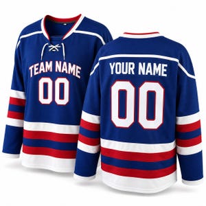 Puede incluir: Dos camisetas de hockey azules con detalles blancos y rojos. La camiseta delantera tiene "TEAM NAME" y el número "00" en blanco. La camiseta trasera tiene "YOUR NAME" y el número "00" en blanco. Ambas camisetas tienen rayas blancas en las mangas y el dobladillo.