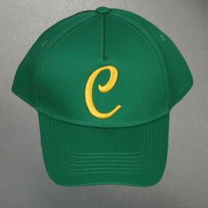 Può includere: Cappellino da baseball verde con visiera curva e una "C" gialla ricamata sul davanti. Il cappellino è realizzato in un tessuto resistente e presenta un bottone sulla parte superiore. Uno stile classico per l'abbigliamento casual.