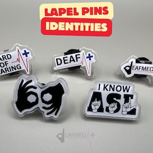 Może przedstawiać: Kolekcja przypinek z różnymi wzorami i tekstami, w tym "Hard of Hearing", "Deaf" i "I Know ASL". Każda przypinka ma symbol medyczny i przezroczyste, błyszczące wykończenie. Przypinki mają reprezentować tożsamości.