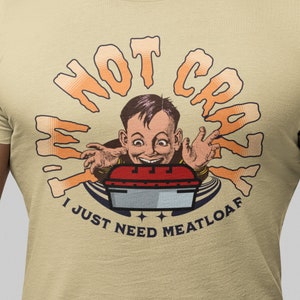 May include: A beige t-shirt with a graphic of a cartoon boy with a surprised expression. The graphic says "I'm not crazy I just need meatloaf".