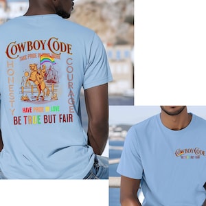 May include: Two light blue t-shirts with the text "COWBOY CODE" in brown, yellow, green, and red. The text is surrounded by a rainbow-colored arc. The left t-shirt has additional text: "TAKE PRIDE IN YOUR WORK", "HONESTY", "COURAGE", "HAVE PRIDE IN LOVE", and "BE TRUE BUT FAIR".