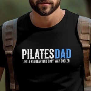 May include: A black t-shirt with white text that reads "PILATESDAD LIKE A REGULAR DAD ONLY WAY COOLER".