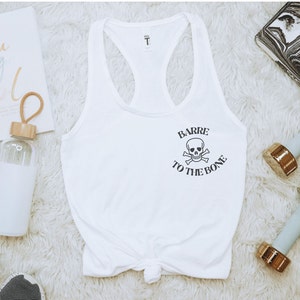 May include: White tank top with a black skull and crossbones graphic and the text "Barre to the Bone".