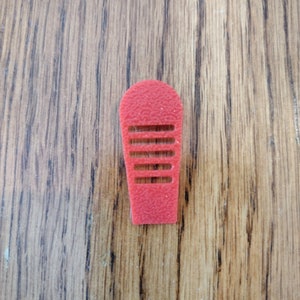 May include: A red plastic finger guard with a series of horizontal slots. The guard is designed to protect the finger from injury.