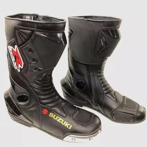 May include: A pair of black leather motorcycle boots with a silver buckle and a yellow "Suzuki" logo. The boots have a zip on the side and a protective shin guard.