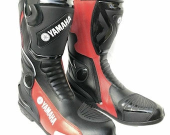 May include: A pair of black and red motorcycle boots with the Yamaha logo on the side. The boots have a zipper on the side and a buckle on the top.