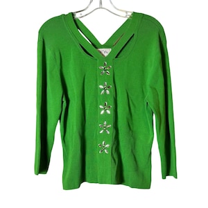 May include: A green long-sleeved sweater with a criss-cross detail at the neckline and a row of silver and green flower-shaped buttons down the front.