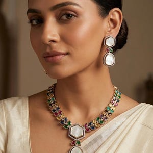 May include: A gold necklace and earring set. The necklace and earrings feature a white, iridescent central stone. The necklace and earrings are decorated with colourful gemstones in various shapes and sizes, creating a vibrant and elegant appearance.