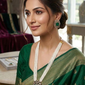 May include: A multi-strand white seed pearl necklace featuring a large square pendant with a central green stone surrounded by clear crystals, paired with matching square stud earrings containing a green stone and clear crystal border.
