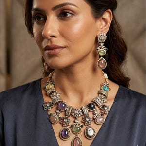 May include: A woman wearing a multi-gemstone necklace and matching earrings. The necklace features a variety of colorful gemstones, including amethyst, pink quartz, and turquoise, set in a gold-toned metal. The earrings have a similar design, with dangling gemstones.