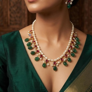 May include: A necklace featuring a strand of white pearls accented with alternating teardrop-shaped green and red gemstones in gold settings. A matching earring with a single green gemstone and a white pearl is visible on the earlobe.
