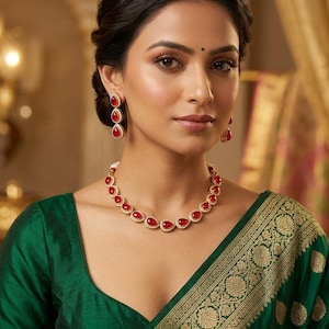 May include: A woman wearing a gold necklace and matching earrings with red teardrop-shaped stones. The jewellery is set against a green silk blouse and a patterned gold and green sari.