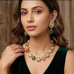 May include: A gold-toned necklace and matching drop earrings featuring multi-colored cabochon stones, including green, orange, and pale pink, interspersed with small floral-shaped clusters of clear crystals and tiny white pearls.