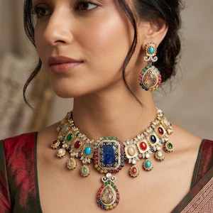 May include: A gold-toned necklace and matching drop earring set featuring a central rectangular blue stone surrounded by smaller multi-colored cabochon stones including red, green, turquoise, and clear gems, with intricate filigree metalwork.