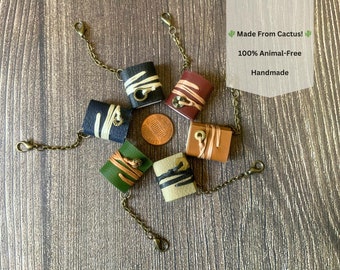 May include: Six small leather-bound journals with a chain and clasp closure. Each journal is a different color: green, brown, black, tan, and two shades of brown. The journals are made from cactus and are 100% animal-free. The text on the image reads "Made From Cactus! 100% Animal-Free Handmade."