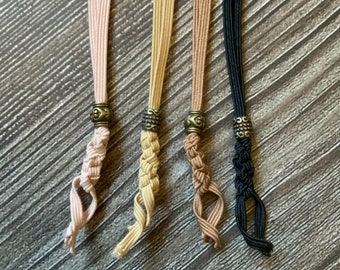 May include: Four braided elastic cords with metal beads at the ends. The cords are in shades of pink, beige, brown, and black.