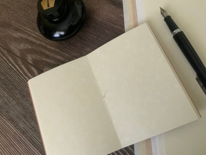 A single travelers notebook insert laying on a wooden surface.  The notebook insert is open, showcasing the speckled patterns of the animal-free parchment paper.