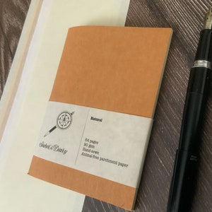A single travelers notebook insert laying on a wooden surface.  The cover is made of a brown vegan leather, also known as washable paper.  It has a smooth texture on one side and a rougher texture on the other side.