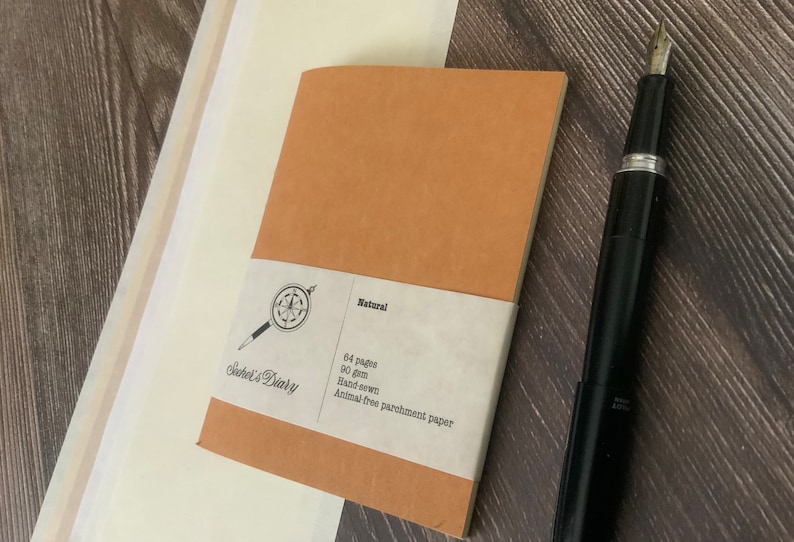A single travelers notebook insert laying on a wooden surface.  The cover is made of a brown vegan leather, also known as washable paper.  It has a smooth texture on one side and a rougher texture on the other side.