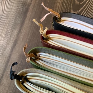 The decorative tails of 4 notebook insert connectors extending from the bottom of 4 travelers notebook journal covers that are filled with notebook inserts.
