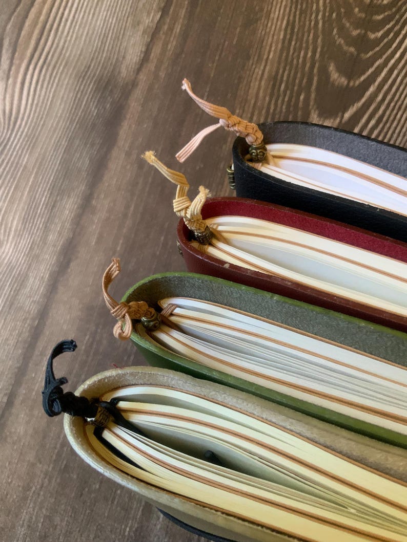 The decorative tails of 4 notebook insert connectors extending from the bottom of 4 travelers notebook journal covers that are filled with notebook inserts.