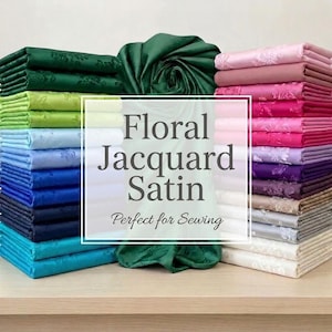 May include: Stacks of colorful floral jacquard satin fabric in shades of green, blue, pink, purple, and white. The fabric is arranged on a wooden surface. The image includes the text "Floral Jacquard Satin".