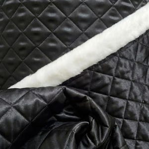 May include: Close-up of black quilted fabric with a diamond pattern. A strip of white faux fur is diagonally across the image. The fabric has a shiny, satin-like appearance.