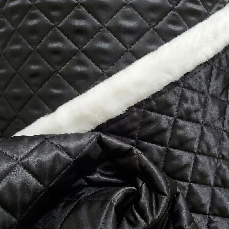 May include: Close-up of black quilted fabric with a diamond pattern. A strip of white faux fur is diagonally across the image. The fabric has a shiny, satin-like appearance.