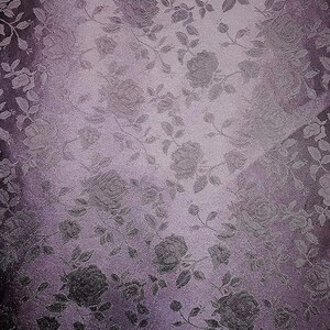 May include: A textured fabric with a floral pattern featuring roses and leaves in shades of purple and gray. The design has a subtle sheen, creating a vintage or romantic aesthetic. The fabric's color gradient adds depth to the overall design.