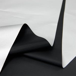 May include: A close-up shot of a folded sheet of white paper revealing a black surface underneath. The paper has a smooth texture, and the contrast between the white and black creates a striking visual effect. The paper is folded in a zig-zag pattern.
