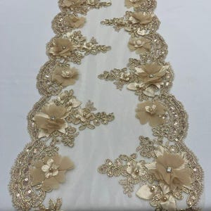 Puede incluir: Camino de mesa de encaje beige con adornos florales y lentejuelas. El camino de mesa presenta flores de tela 3D con detalles de perlas y pedrería. Los bordes están festoneados y decorados con lentejuelas, creando un diseño delicado y elegante.