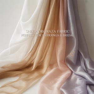 May include: Sheer organza fabric in a gradient of colors, including white, tan, pink, and lavender. The fabric is draped, creating soft folds and a flowing appearance. Text on the fabric reads: SHEER ORGANZA FABRIC PERFECT FOR WEDDINGS & BRIDAL.