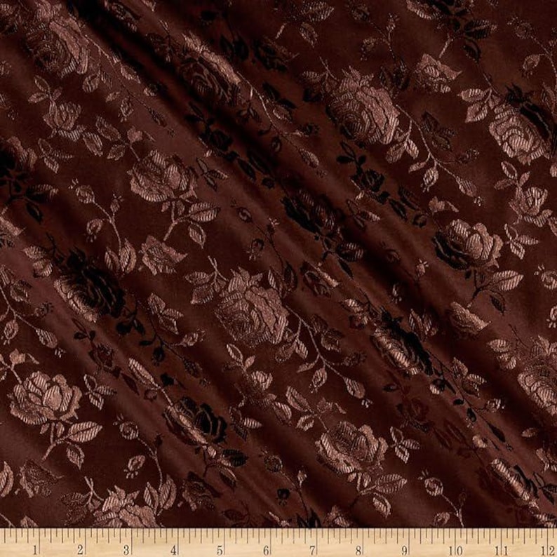 May include: Close-up of a dark brown fabric with a floral pattern. The fabric features a repeating design of roses and leaves in a slightly lighter shade of brown, creating a textured effect. The fabric is likely used for upholstery or drapery.
