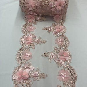 Könnte beinhalten: Eine Rolle rosafarbener Spitzenborte mit floralen Verzierungen. Der Besatz weist zarte, dreidimensionale rosa Stoffblumen, Pailletten und Perlenakzente auf. Die Spitze hat einen gewellten Rand und eignet sich für verschiedene Bastelprojekte.