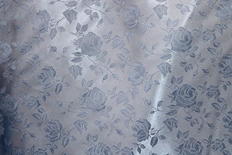 May include: A close-up of a fabric with a repeating pattern of light blue roses and leaves. The roses are detailed with shading, and the fabric has a subtle sheen. The overall effect is elegant and floral.