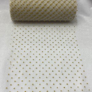 May include: A roll of white tulle fabric with gold glitter dots. The fabric is rolled up and the glitter dots are visible on the surface.
