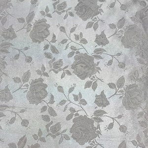 May include: A close-up of a fabric with a repeating pattern of roses and leaves in a light gray color. The roses are in full bloom and the leaves are detailed. The fabric has a subtle sheen.