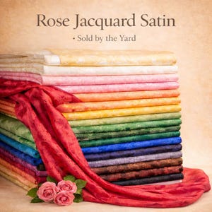 May include: A stack of Rose Jacquard Satin fabric in various colors, including yellow, pink, orange, green, and blue. A red satin fabric is draped over the stack, with three pink roses at the bottom. The text "Rose Jacquard Satin" and "Sold by the Yard" is visible.