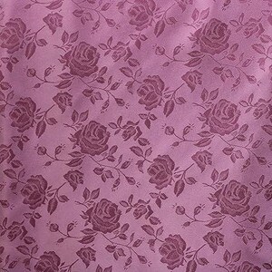May include: A close-up of a mauve fabric with a repeating pattern of roses and leaves. The roses are in a darker shade of mauve, creating a subtle contrast. The fabric has a slight sheen.