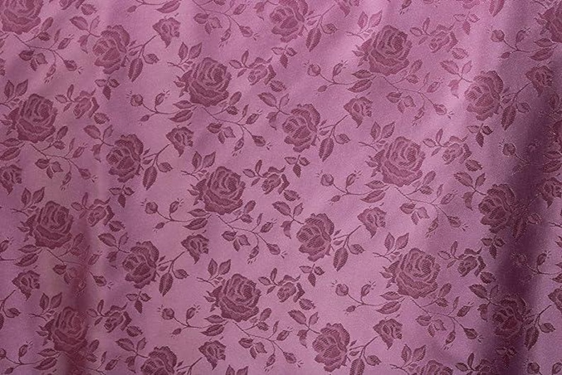 May include: A close-up of a mauve fabric with a repeating pattern of roses and leaves. The roses are in a darker shade of mauve, creating a subtle contrast. The fabric has a slight sheen.