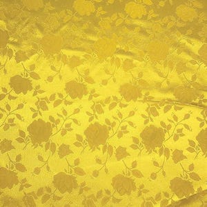 May include: Close-up of a golden yellow fabric with a repeating floral pattern. The design features roses and leaves in a tone-on-tone effect, creating a textured appearance. The fabric has a slight sheen.