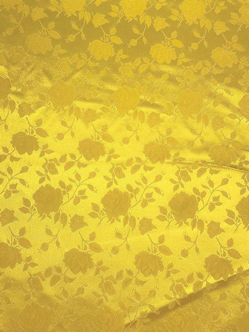 May include: Close-up of a golden yellow fabric with a repeating floral pattern. The design features roses and leaves in a tone-on-tone effect, creating a textured appearance. The fabric has a slight sheen.