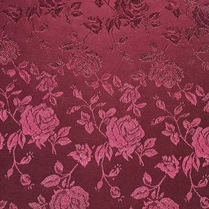 May include: Burgundy fabric with a repeating pattern of roses and leaves. The roses are a lighter shade of burgundy, creating a subtle contrast. The fabric has a textured appearance, with the floral design slightly raised.