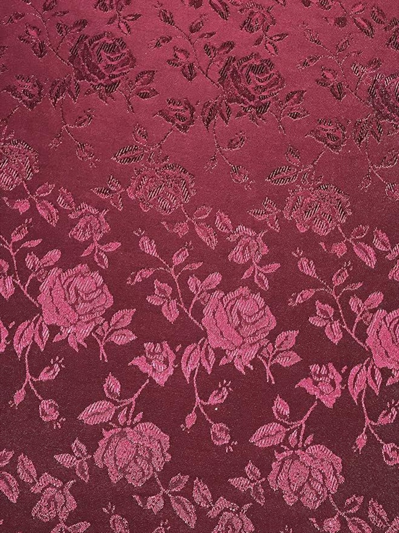May include: Burgundy fabric with a repeating pattern of roses and leaves. The roses are a lighter shade of burgundy, creating a subtle contrast. The fabric has a textured appearance, with the floral design slightly raised.